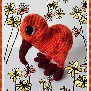 May include: A crocheted kiwi bird toy with orange and red yarn. The toy has a long, curved beak and small, black eyes. The toy is sitting on a white background with black and yellow flowers.