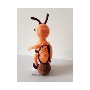 May include: A crocheted orange and brown ant toy with a brown crocheted ball for a bottom. The ant has a black eye and a brown crocheted head.