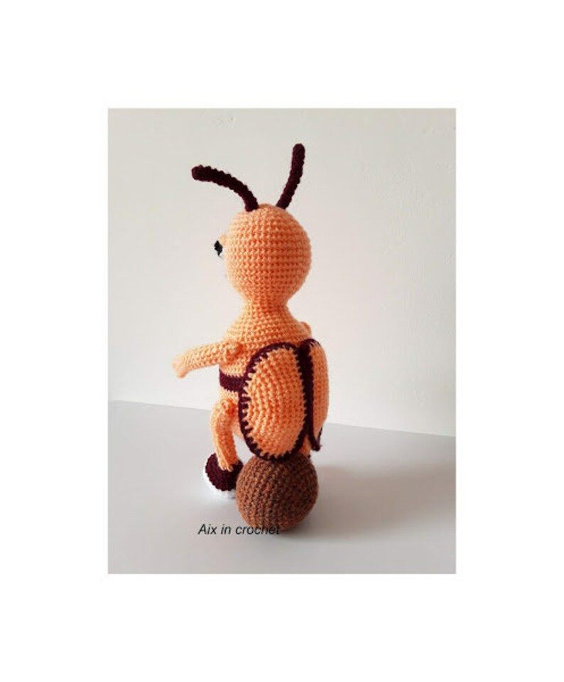 May include: A crocheted orange and brown ant toy with a brown crocheted ball for a bottom. The ant has a black eye and a brown crocheted head.
