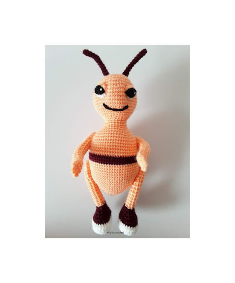 May include: A crocheted bee plush toy with orange and brown yarn. The bee has a smiling face with black eyes and a black mouth. The bee has white feet.