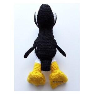 Op de afbeelding: Een zwart-witte gehaakte pingu&iuml;n met gele voeten. De pingu&iuml;n staat op een wit oppervlak. De tekst "Aix in crochet" is zichtbaar rechtsonder in de afbeelding.