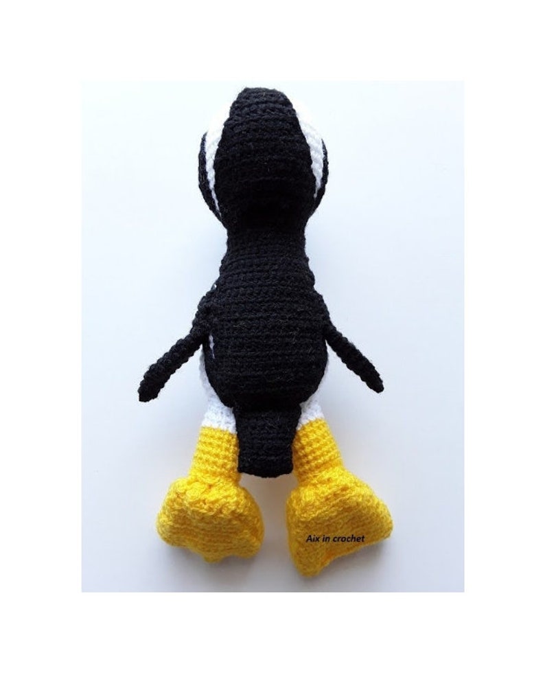 Op de afbeelding: Een zwart-witte gehaakte pingu&iuml;n met gele voeten. De pingu&iuml;n staat op een wit oppervlak. De tekst "Aix in crochet" is zichtbaar rechtsonder in de afbeelding.