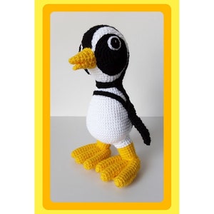 Op de afbeelding: Een gehaakt pingu&iuml;n speelgoed met zwart-witte strepen, een gele snavel en gele voeten. De pingu&iuml;n staat op een wit oppervlak.