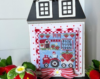 May include: A red and white gingham and polka dot patterned frame with a cross-stitch design of a red tractor pulling a wagon full of strawberries. The sign reads "Pick Your Own".