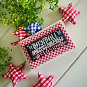 May include: A white card with a red and white gingham pattern border. The card features a cross-stitch design of a baseball scoreboard with the text "Baseball is my favorite season". The card is surrounded by red and white gingham stars.