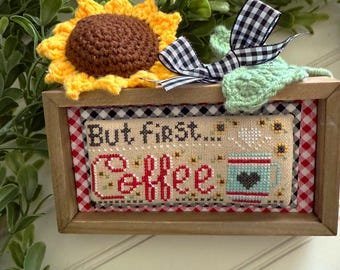 May include: A framed cross-stitch with a red and white gingham border. The cross-stitch reads "But first, coffee" and features a coffee cup with a heart on it.
