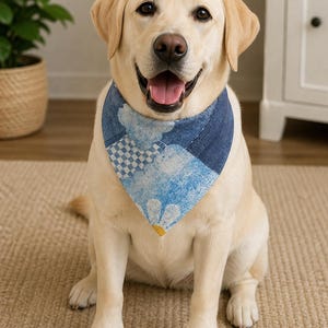 Peut inclure: Un Labrador Retriever souriant porte un bandana bleu et blanc à motifs. Le bandana présente un motif patchwork avec des nuages et un motif à carreaux. Le chien est assis sur un tapis beige.