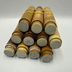 Może przedstawiać: Kolekcja cylindrycznych przedmiotów w odcieniach jasnobrązowym i beżowym, spiętych żółtą gumką. Końce cylindrów są zakończone jasnoszarym materiałem, tworząc kontrast.