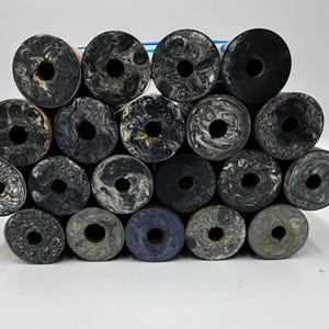 May include: A collection of seventeen cylindrical objects arranged in a stack, each featuring a unique marbled pattern in shades of black, grey, and white. Every cylinder has a circular hole in the centre, revealing a brown interior core.