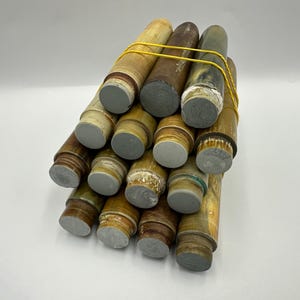 Może przedstawiać: Kolekcja cylindrycznych przedmiotów w odcieniach brązu, beżu i szarości, spiętych żółtą gumką. Każdy cylinder ma szary, płaski koniec. Przedmioty wydają się być wykonane z drewna lub podobnego materiału.