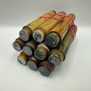 Puede incluir: Una colección de sellos de lacre antiguos. Los sellos tienen mangos de madera y cabezas de sello grises o marrones con varios diseños en relieve. Una banda de goma roja sujeta los sellos.