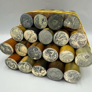 May include: A bundle of cylindrical objects with swirled patterns on the ends. The cylinders have a mix of colors, including brown, yellow, gray, and cream. They are bound together with a yellow cord.