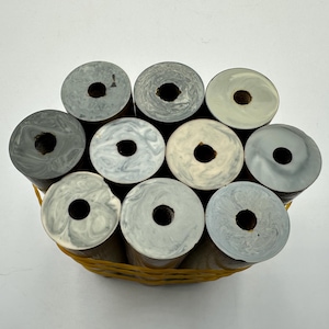 May include: A collection of ten cylindrical objects with marbled gray, white, and cream-colored tops, each featuring a central circular hole. The cylinders are bundled together and secured by a bright yellow rubber band around their exterior.