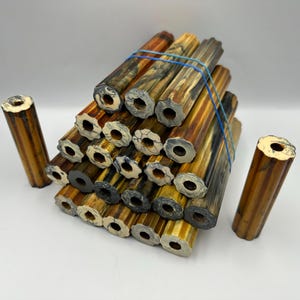 Puede incluir: Una colección de espigas de madera con un acabado natural y multicolor. Las espigas son cilíndricas con una abertura en forma de estrella en cada extremo. Una banda elástica azul asegura la pila. Dos espigas adicionales se colocan cerca.