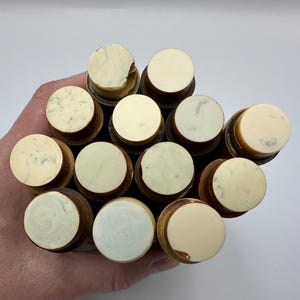 Könnte beinhalten: Eine Ansammlung von Holz-Flaschenverschlüssen mit elfenbeinfarbenen Oberteilen. Die Verschlüsse haben ein kreisförmiges Design und werden zusammengehalten. Die Oberteile haben ein glattes, leicht strukturiertes Aussehen.