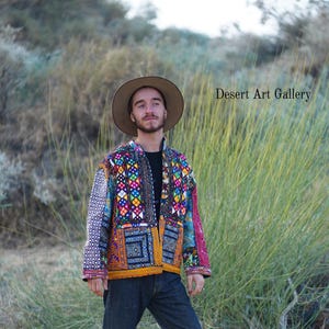 May include: A colorful, patchwork jacket with geometric patterns and a brown hat. The jacket features a variety of colors including blue, yellow, pink, and orange. The text "Desert Art Gallery" is visible in the background.
