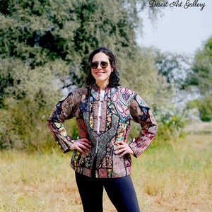 May include: A colorful, patterned jacket with a zipper, paired with black leggings. The jacket features a mix of paisley and floral designs in various colors. The text "Desert Art Gallery" is visible in the upper right corner.