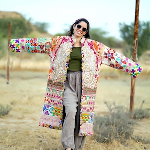 May include: A vibrant, embroidered coat with a patchwork design. The coat showcases various patterns and colours, including pink, blue, and gold. The text "Desert Art Gallery" is visible in the upper right corner.