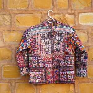 Op de afbeelding: Een kleurrijke jas met lange mouwen, ingewikkelde borduursels en spiegelaccenten. De jas heeft een knoopsluiting en een levendig patchwork-ontwerp in tinten rood, oranje, groen en blauw. De tekst "Desert Art Gallery" is rechtsboven zichtbaar.