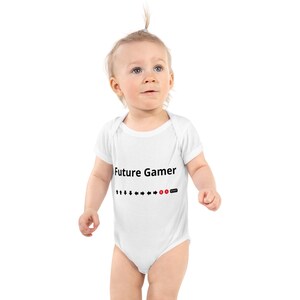 May include: White baby onesie with the text "Future Gamer" in black. Below the text are black arrows, a red "B" button, and a red "Start" button. The onesie is worn by a baby.