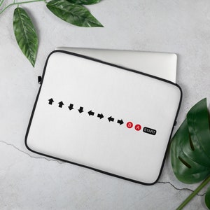 May include: White laptop sleeve with a black border. The design features a series of black arrows and the words "START", and the letters "A" and "B" in red. The sleeve is designed to protect a laptop.