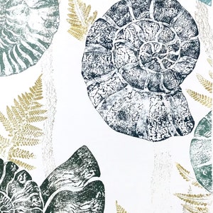 May include: A white background with a print of various shades of green and gold. The print features several stylised ammonite fossils and fern leaves.