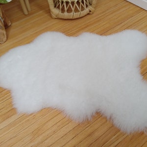May include: A white fluffy sheepskin rug with a cloud-like shape. The rug is on a wooden floor.