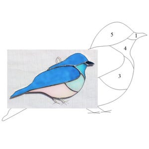 May include: A stained glass bird with blue, pink, and white glass pieces. The bird is in a standing position with its wings spread out. A pattern for the stained glass bird is shown next to the finished piece.