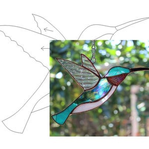 May include: A stained glass hummingbird with iridescent wings and a copper wire frame. The hummingbird is hanging from a chain and is in front of a blurred green background.