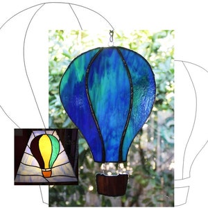 May include: A stained glass hot air balloon with blue and green glass. The balloon is hanging from a window and the background is blurred.