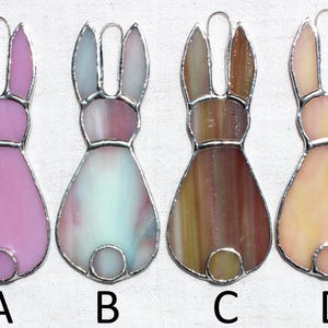 May include: Four stained glass bunny ornaments in shades of pink, blue, brown, and peach. Each bunny has a silver-colored metal outline and a loop for hanging. The ornaments are labeled A, B, C, and D.