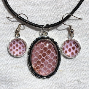 May include: A pink and brown snake skin pattern necklace and earrings set with a black leather cord.
