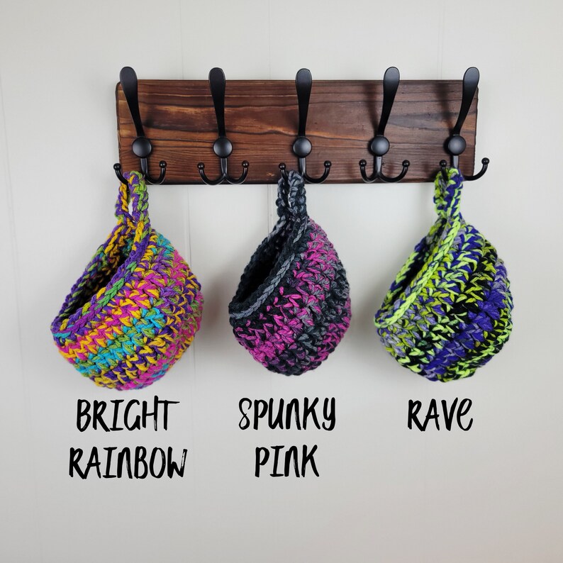 May include: Three crocheted hanging baskets in bright colours. The baskets are labelled "Bright Rainbow", "Spunky Pink", and "Rave".