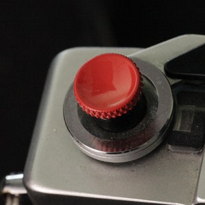 May include: A silver Canon camera with a red button and the text "Canon" and "OL72" printed on the body.