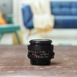 May include: A black camera lens with a silver ring and markings. The lens is sitting on a wooden surface.