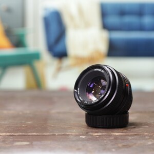 May include: A black Minolta MC Rokkor-X 50mm f/1.7 lens with a silver ring around the lens barrel.