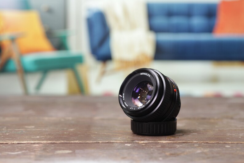 May include: A black Minolta MC Rokkor-X 50mm f/1.7 lens with a silver ring around the lens barrel.