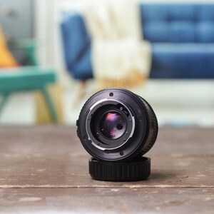 May include: A black camera lens with a silver ring around the lens. The lens is sitting on a wooden table.