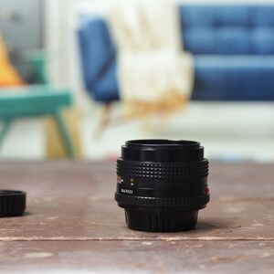 May include: A black camera lens with a black lens cap on a wooden table. The lens has a silver ring around it and a red dot on the side.