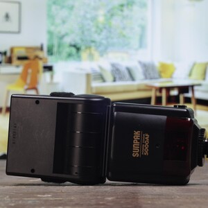 Może przedstawiać: Czarna lampa błyskowa z złotą etykietą z napisem "SUNPAK Auto Zoom 5000AF".