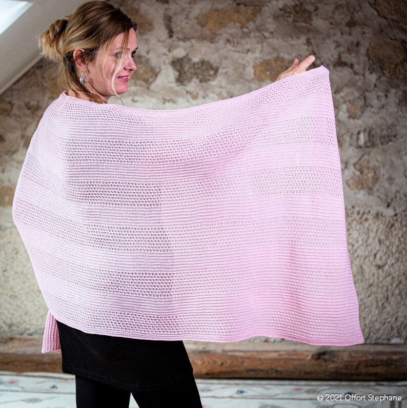 May include: A pink knitted shawl with a delicate openwork pattern. The shawl is draped over a person's shoulders and is held out in front of them.