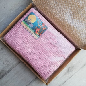 May include: A pink knitted alpaca wool blanket in a cardboard box with a label that reads "Latitude Laine" and "Fabrication Artisanale Auvergne".