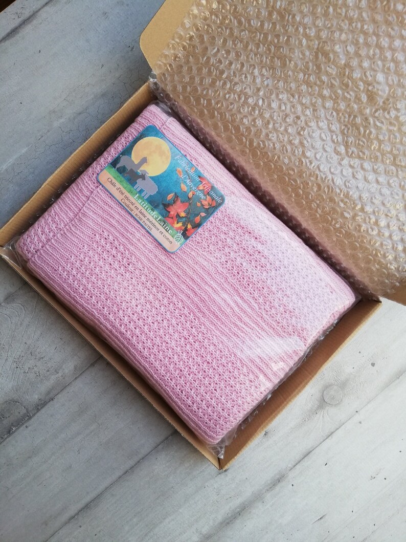 May include: A pink knitted alpaca wool blanket in a cardboard box with a label that reads "Latitude Laine" and "Fabrication Artisanale Auvergne".