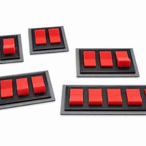 May include: A collection of red toggle switches on black and gray rectangular bases. The switches are arranged in various configurations, from single switches to arrays of six.