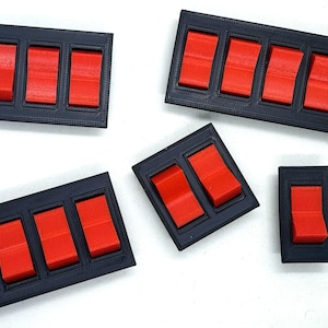 May include: Several black rectangular switch panels with bright red switches. The panels vary in size, with configurations of one, two, three, four, and five switches. The switches are in the on position.