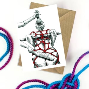 May include: Greeting card with a black and red illustration of a person tied up with rope, being spanked with a paddle that says "SPANK". The card is inside a brown envelope, with blue and purple rope in the foreground.