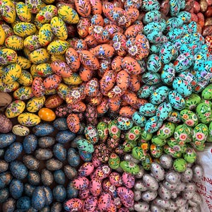 May include: A large collection of hand-painted wooden eggs in various colours and patterns. The eggs are arranged in a circular pattern, with the colours and patterns radiating outwards from the centre. The eggs are all about the same size, and they are all decorated with intricate floral designs.
