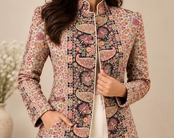 May include: A long-sleeved jacket featuring a high collar and white piping. The garment displays a dense floral pattern in shades of pink, green, and cream, with a prominent black vertical panel down the front adorned with intricate paisley motifs.