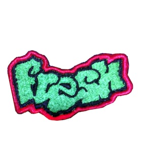 May include: Green embroidered patch with the word "Trash" in a graffiti style font. The patch has a red outline.