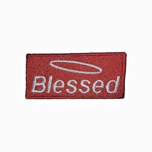 May include: Red rectangular embroidered patch with a white halo above the word "Blessed".